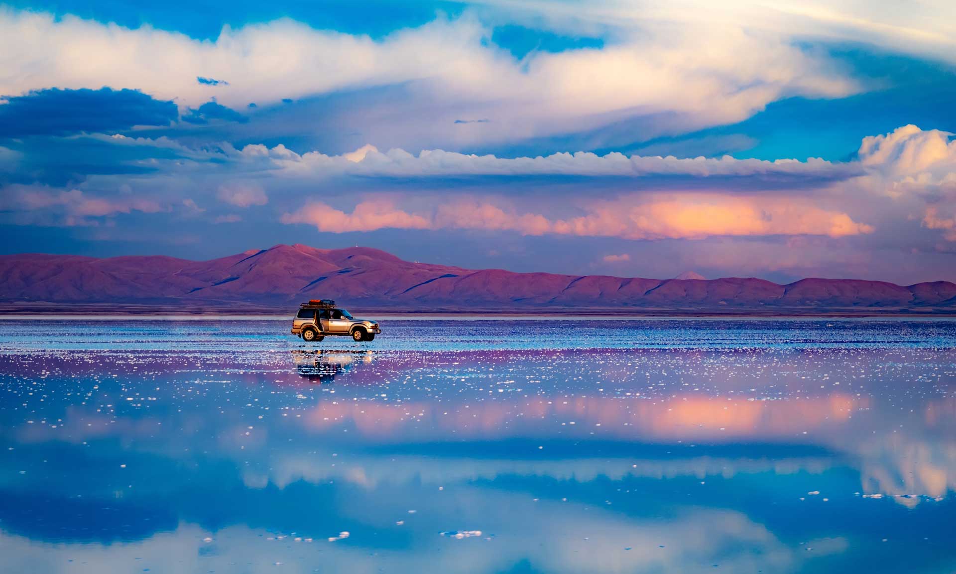 Car standing in middle of salt flat reflecting blue sky, Salar de Uyuni, Bolivia